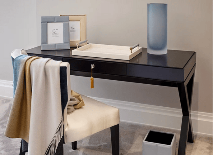 A desk top set up in a luxury home with leather photo frames a decorative serving tray blue vase and multi coloured cashmere throw